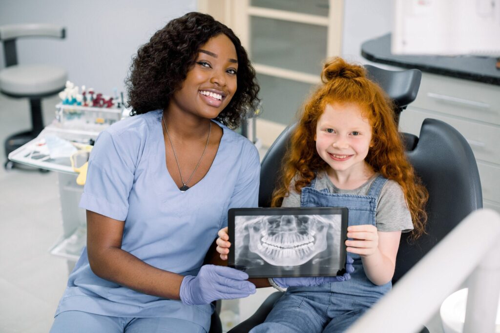 Dental professional and child patient holding a tablet displaying a dental X-ray in a clinic.