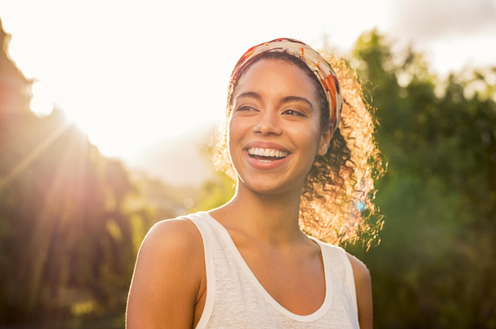 Person wearing a white sleeveless top and headscarf standing outdoors in sunlight