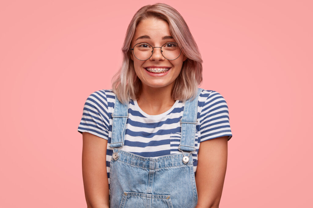 Person wearing a striped t-shirt and denim overalls against a pink background.