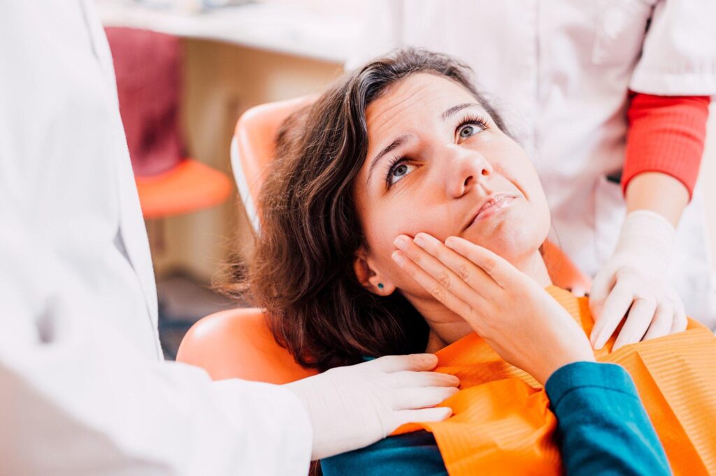 Patient sitting in a dental chair with hands near mouth, assisted by dental professionals